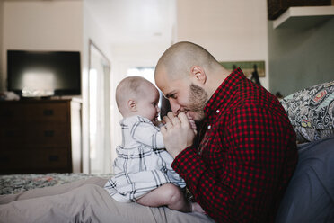 Seitenansicht des Vaters, der mit seiner Tochter spielt, während er zu Hause auf dem Bett sitzt - CAVF51114