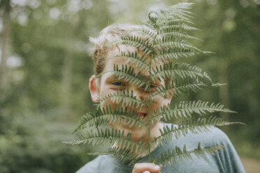 Close-up portrait of cheerful boy holding fern against face - CAVF51125