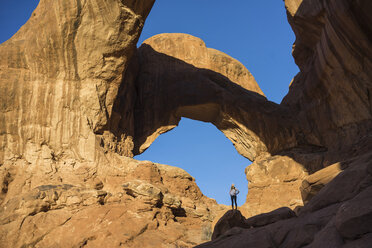 Full length of woman standing on rock formation at Arches National Park against clear blue sky - CAVF51135
