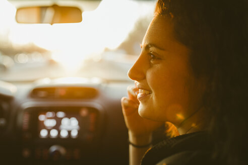Lächelnde junge Frau, die bei Sonnenuntergang im Auto unterwegs ist - CAVF51139