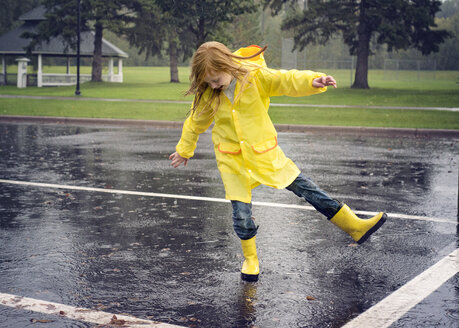 Verspieltes Mädchen trägt Regenmantel beim Tanzen auf der Straße bei Regen - CAVF51143
