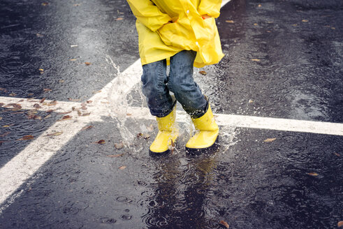 Niedriger Ausschnitt eines Mädchens, das während des Regens auf die Straße springt - CAVF51145