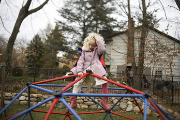 Mädchen in voller Länge mit Hand im Haar auf kuppelförmigem Klettergerüst auf einem Spielplatz im Herbst sitzend - CAVF51151