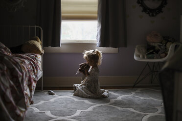 Side view of girl playing while sitting on carpet against window in bedroom - CAVF51152