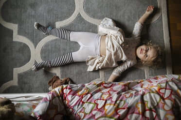 Overhead-Porträt eines Mädchens, das auf einem Teppich im Schlafzimmer liegt - CAVF51154