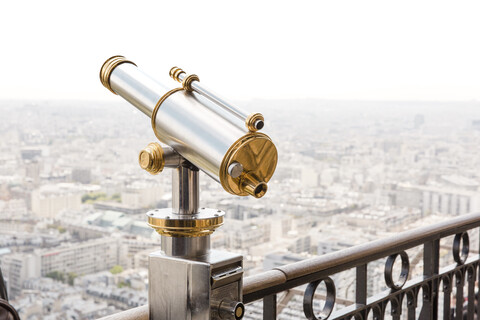 Münzfernglas auf einem Geländer vor einer Stadtlandschaft bei klarem Himmel, lizenzfreies Stockfoto