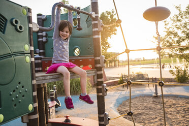 Glückliches Mädchen, das auf einem Spielplatz an einem Spielgerät im Freien spielt - CAVF51218