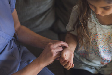 Midsection of female doctor checking pulse of girl while sitting on sofa at home - CAVF51228