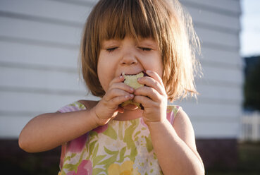 Close-up of girl eating apple while standing against wall - CAVF51241