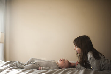 Schwester spielt mit Bruder auf dem Bett liegend gegen die Wand zu Hause - CAVF51242