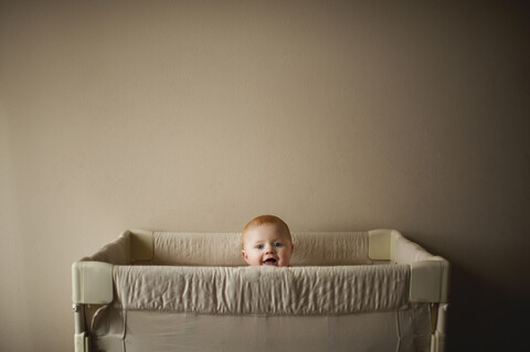 Portrait of baby boy in crib against wall at home stock photo