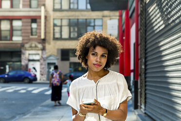 Portrait of woman holding smart phone in city - CAVF51253