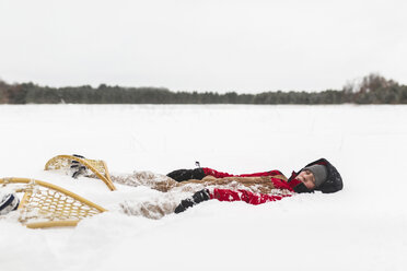 Jugendlicher mit Schneeschuhen auf einem verschneiten Feld vor dem Himmel liegend - CAVF51261