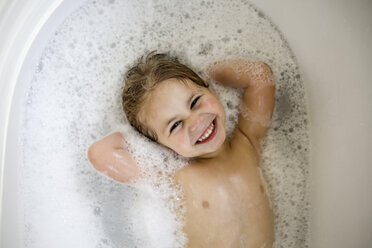 Overhead portrait of cheerful girl with hands behind head lying in bathtub - CAVF51277