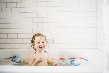 Porträt eines fröhlichen Mädchens beim Baden in einer Badewanne vor einer gefliesten Wand - CAVF51278