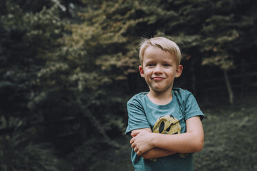 Portrait of confident boy with arms crossed standing at park - CAVF51280