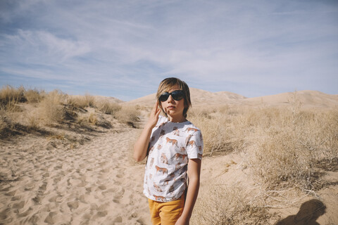 Junge mit Sonnenbrille in der Wüste an einem sonnigen Tag, lizenzfreies Stockfoto