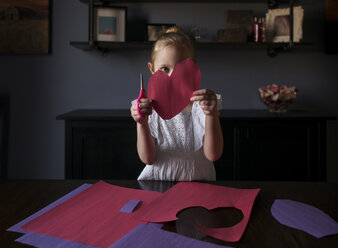 Mädchen Schneiden Handwerk Papiere in Herzform auf dem Tisch zu Hause - CAVF51324