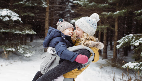 Happy mother carrying daughter in forest during winter stock photo