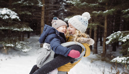 Happy mother carrying daughter in forest during winter - CAVF51358