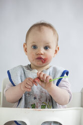 Portrait of smeared baby girl on high chair eating mush - JLOF00272