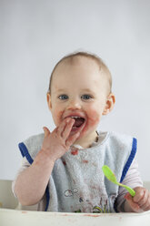 Portrait of smeared baby girl on high chair eating mush - JLOF00274