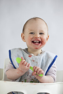 Porträt eines glücklichen kleinen Mädchens mit verschmiertem Gesicht auf einem Hochstuhl - JLOF00275