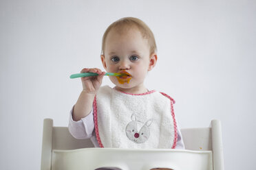 Porträt eines kleinen Mädchens auf einem Hochstuhl, das Brei isst - JLOF00283