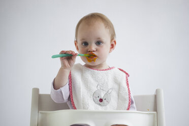 Portrait of baby girl on high chair eating mush - JLOF00283