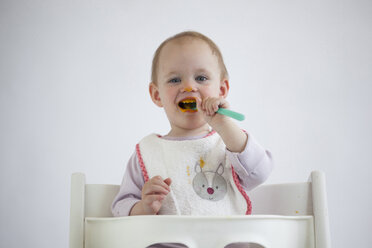 Portrait of smeared baby girl on high chair eating mush - JLOF00284