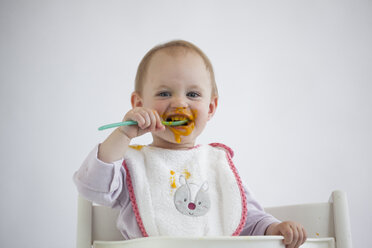 Portrait of smeared baby girl on high chair eating mush - JLOF00286