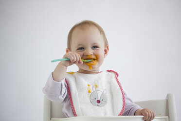 Portrait of smeared baby girl on high chair eating mush - JLOF00287