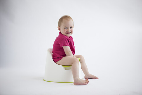 Porträt eines lachenden kleinen Mädchens, das auf dem Töpfchen sitzt, lizenzfreies Stockfoto