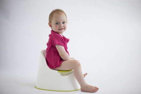 Porträt eines lächelnden kleinen Mädchens, das auf dem Töpfchen sitzt, lizenzfreies Stockfoto