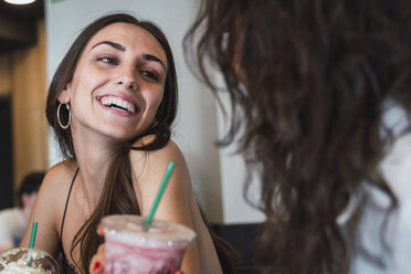 Porträt einer glücklichen jungen Frau in einem Café, die sich mit ihrer Freundin amüsiert - KKAF02808