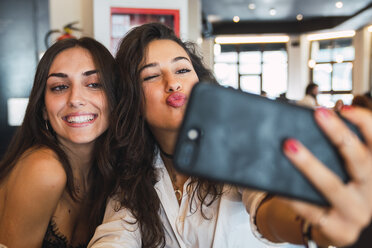 Porträt von zwei Freunden, die ein Selfie mit einem Smartphone in einem Café machen und Spaß haben - KKAF02809