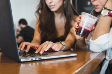 Junge Frau trinkt einen Smoothie in einem Café, während ihr Freund einen Laptop benutzt, Teilansicht - KKAF02810