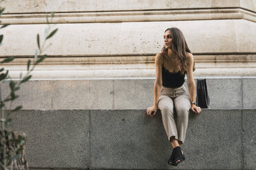 Young woman sitting on a wall waiting - KKAF02827