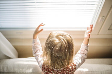 Rückansicht eines blonden kleinen Mädchens am Fenster, das mit dem Sonnenlicht spielt - PSIF00131