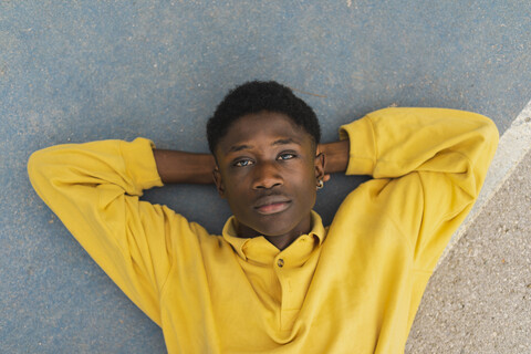 Junger schwarzer Mann auf dem Boden liegend, mit den Händen hinter dem Kopf, lizenzfreies Stockfoto