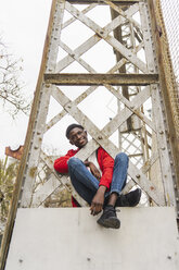 Young man sitting on pillar, smiling - AFVF01885