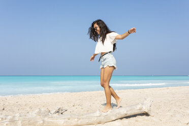 Junge Frau am Strand, die auf einem Baumstamm balanciert - WPEF00977