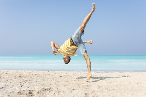 Junger Mann macht einen Purzelbaum am Strand, lizenzfreies Stockfoto