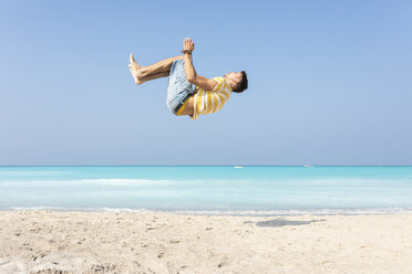 Junger Mann macht einen Purzelbaum am Strand - WPEF00979