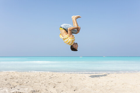 Young man doing a somersault on the beach stock photo