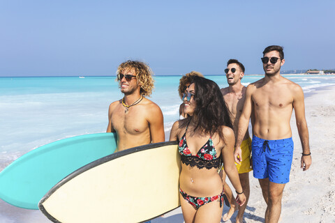 freunde, die Spaß haben, am Strand spazieren gehen, Surfbretter tragen, lizenzfreies Stockfoto