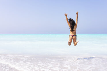 Carefree naked young woman jumping at beach against sea stock photo