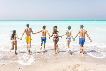 Gruppe von Freunden am Strand, die ins Meer laufen und sich an den Händen halten - WPEF01058