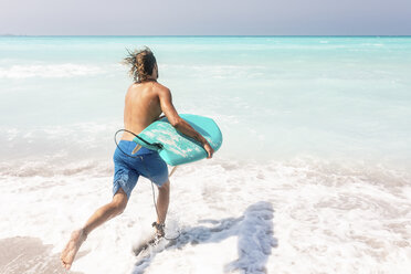 Junger Mann, der mit seinem Surfbrett ins Meer läuft - WPEF01060