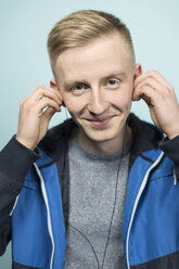 Portrait of smiling young man putting on earphones - VGF00075